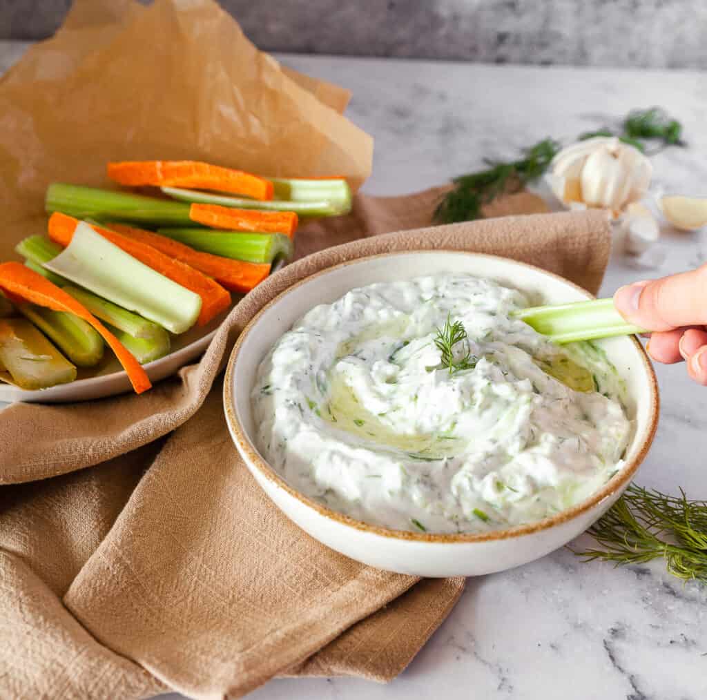 bowl of dill tzatziki with a stick of celery being dipped in 