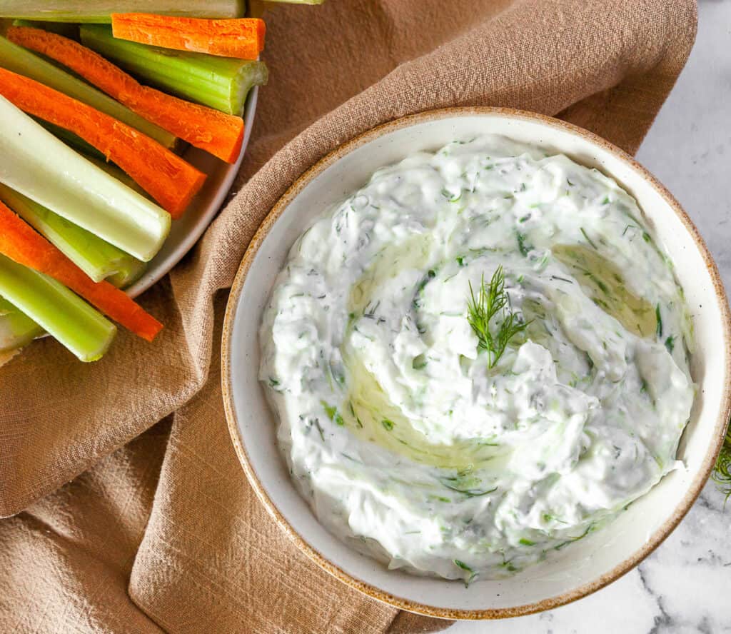 dill tzatziki in a bowl with celery and carrots on a plate