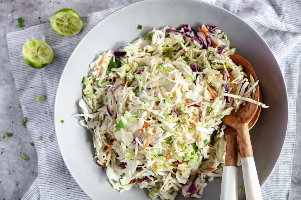 Honey lime coleslaw plated in a bowl with serving spoons