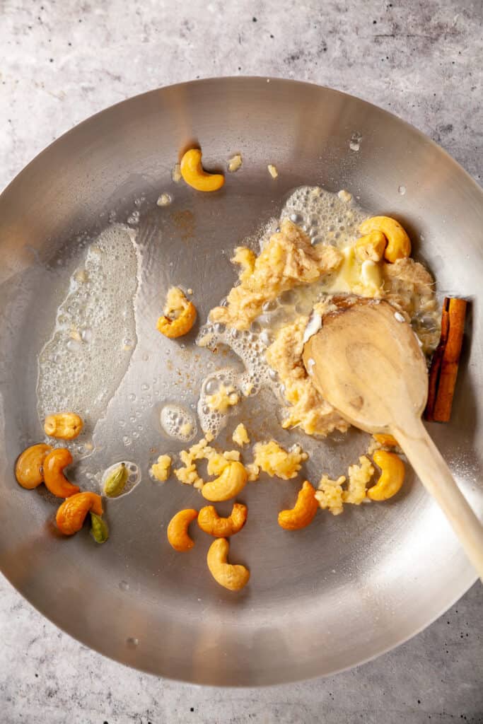 Cashews, garlic, ginger and spices frying in a skillet with butter