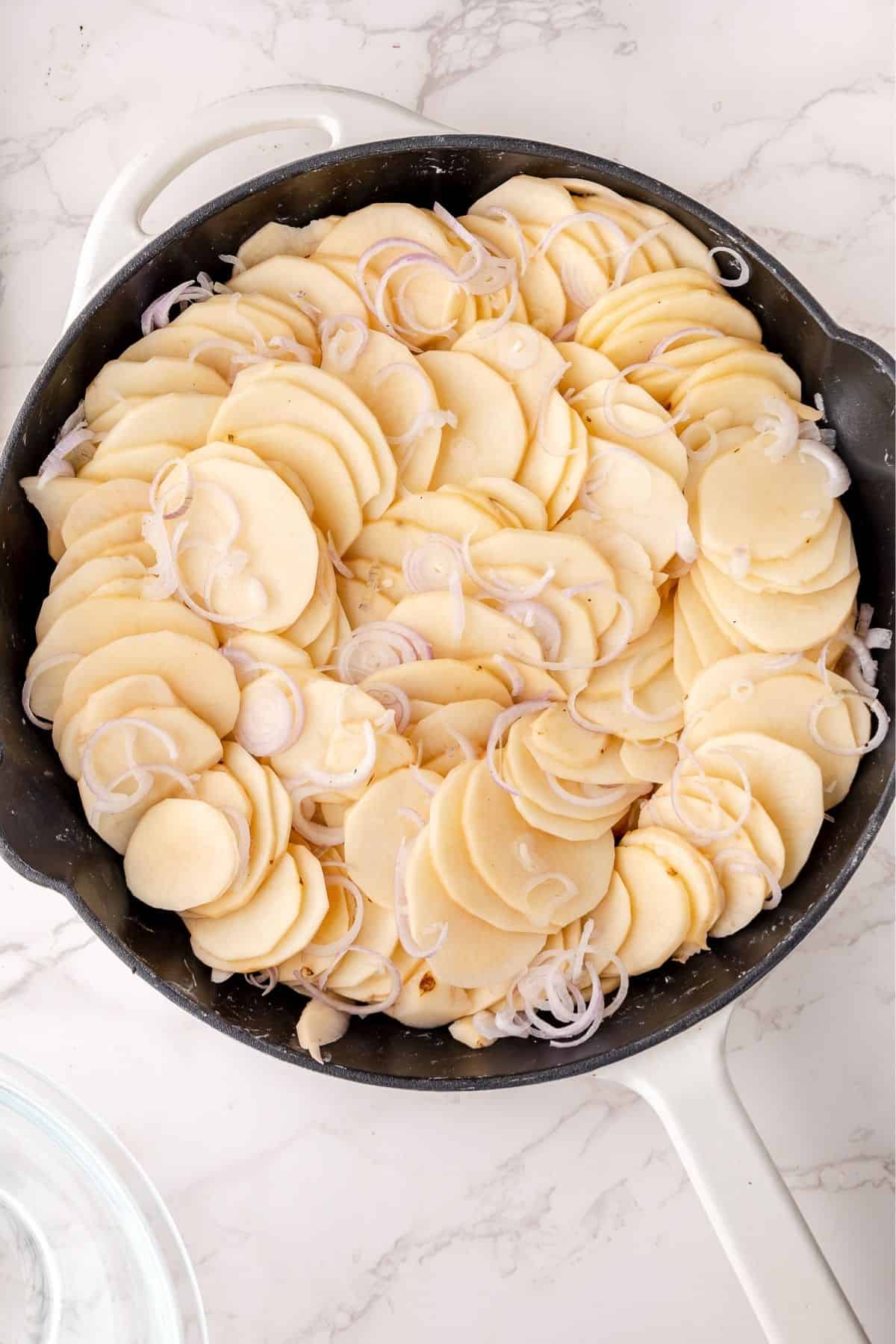 Sliced potatoes and shallots arranged in a cast iron skillet. 