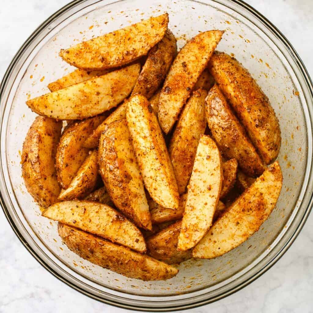 Seasoned potato wedges in a large bowl.
