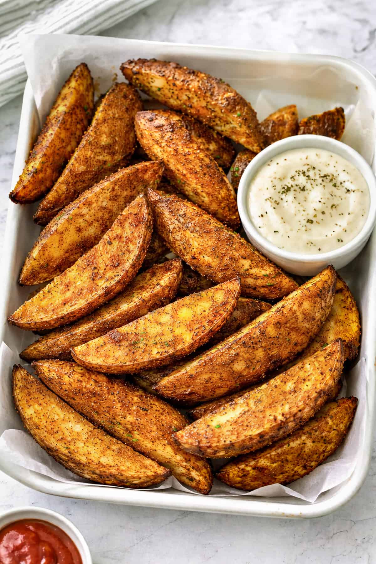 Crispy air fried potato wedges arranged in a serving dish, with ranch dipping sauce and ketchup.