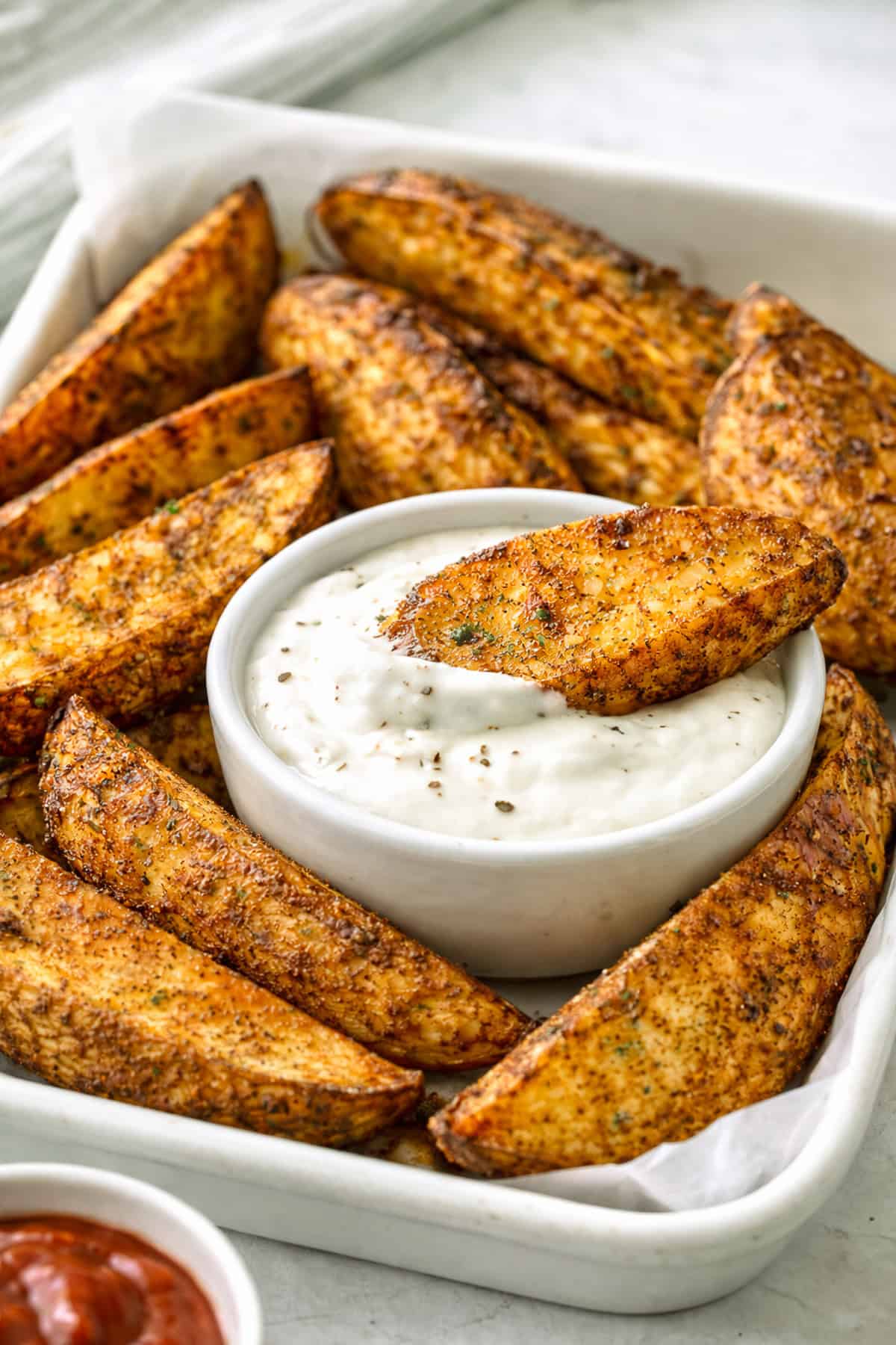 A crispy potato wedge dipping into ranch dipping sauce.
