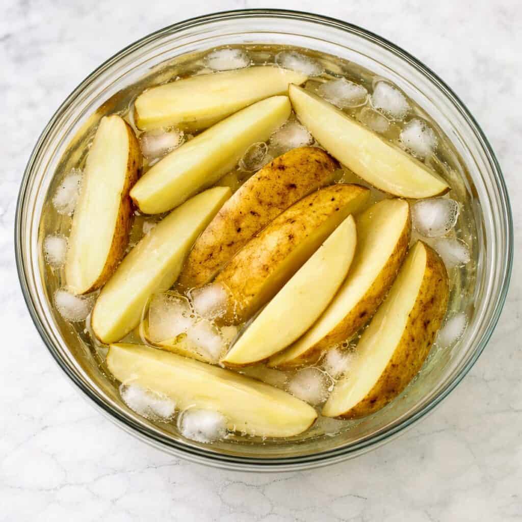 Cut potato wedges soaking in a bowl of ice water.