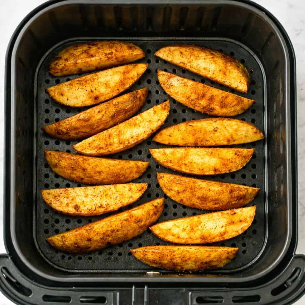 Seasoned potato wedges arranged in an air fryer basket.
