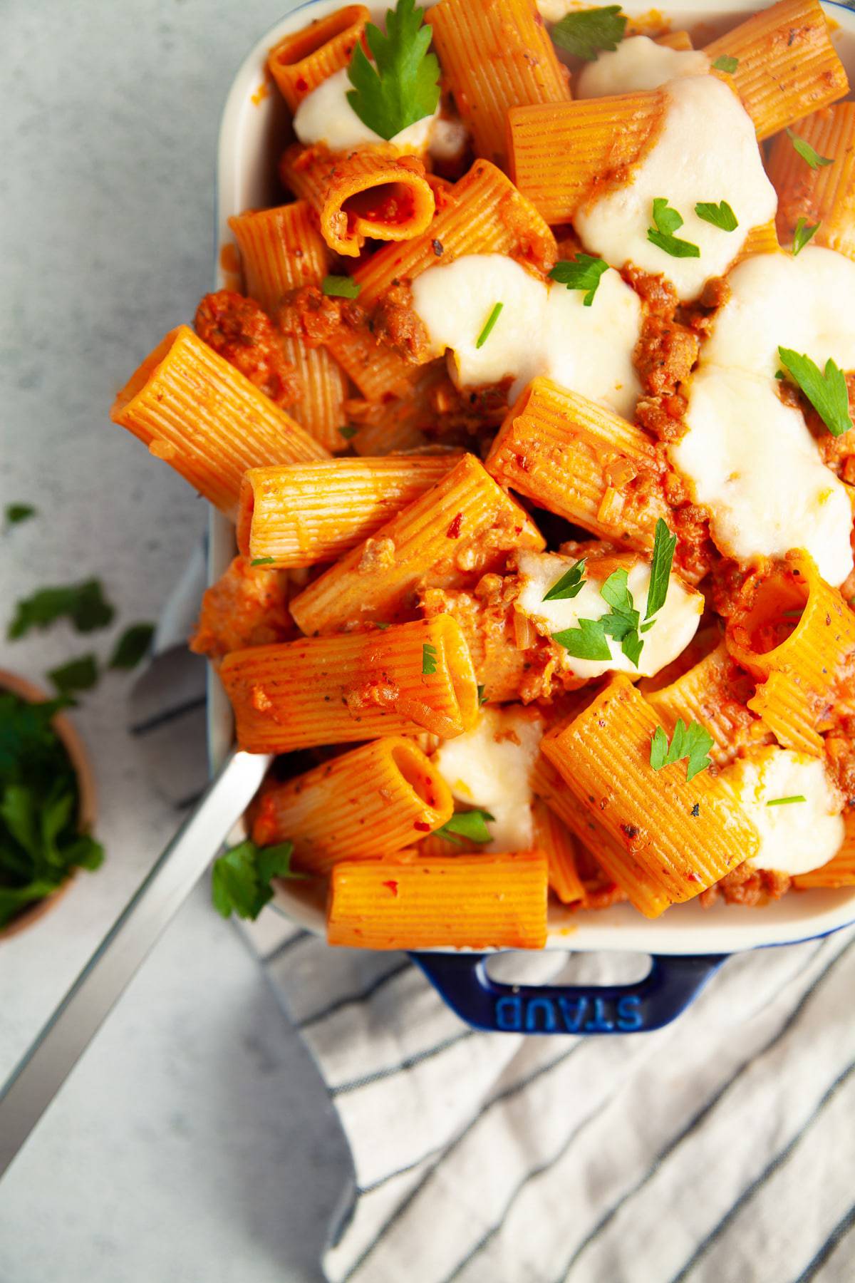 Spicy sausage rigatoni al forno in a baking dish with a spoon, garnished with parsley