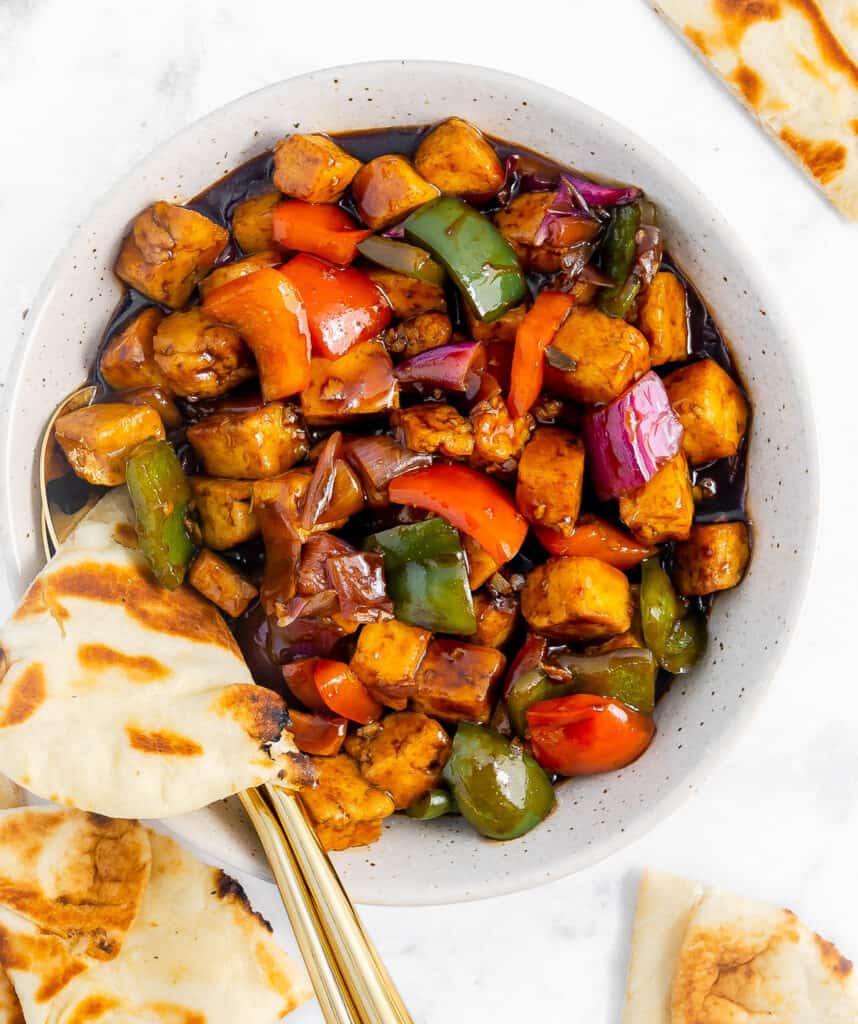 Hakka chilli paneer in a bowl, with triangles of naan