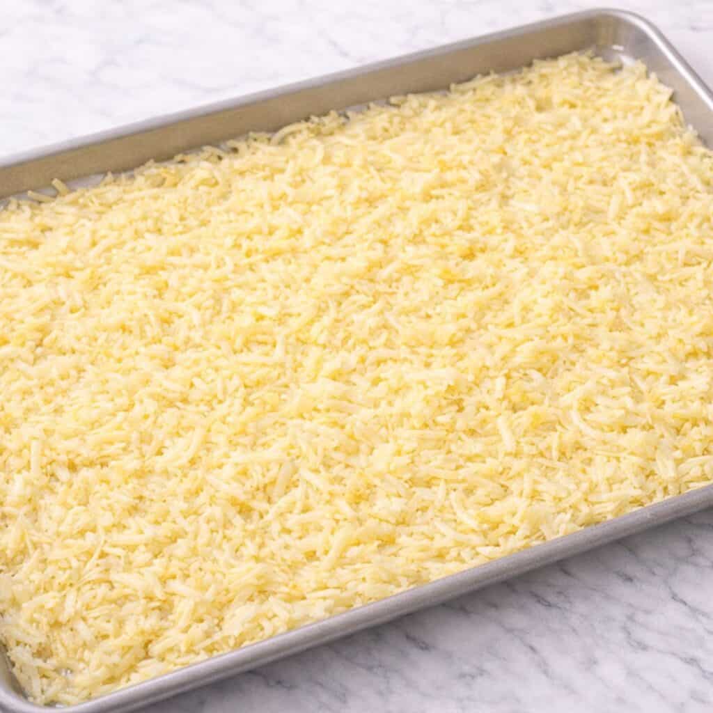 Hash brown potato mixture spread out onto a baking sheet.