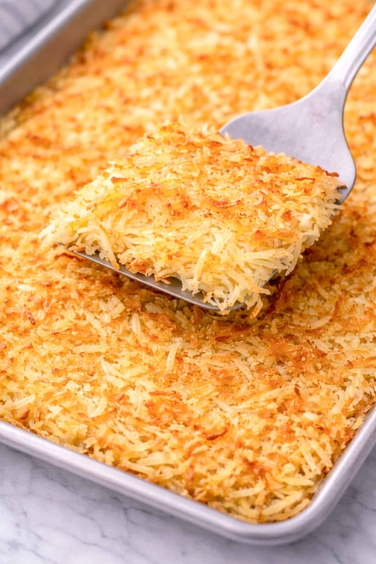IHOP hash browns served on a sheet tray, with a spatula taking out a serving.