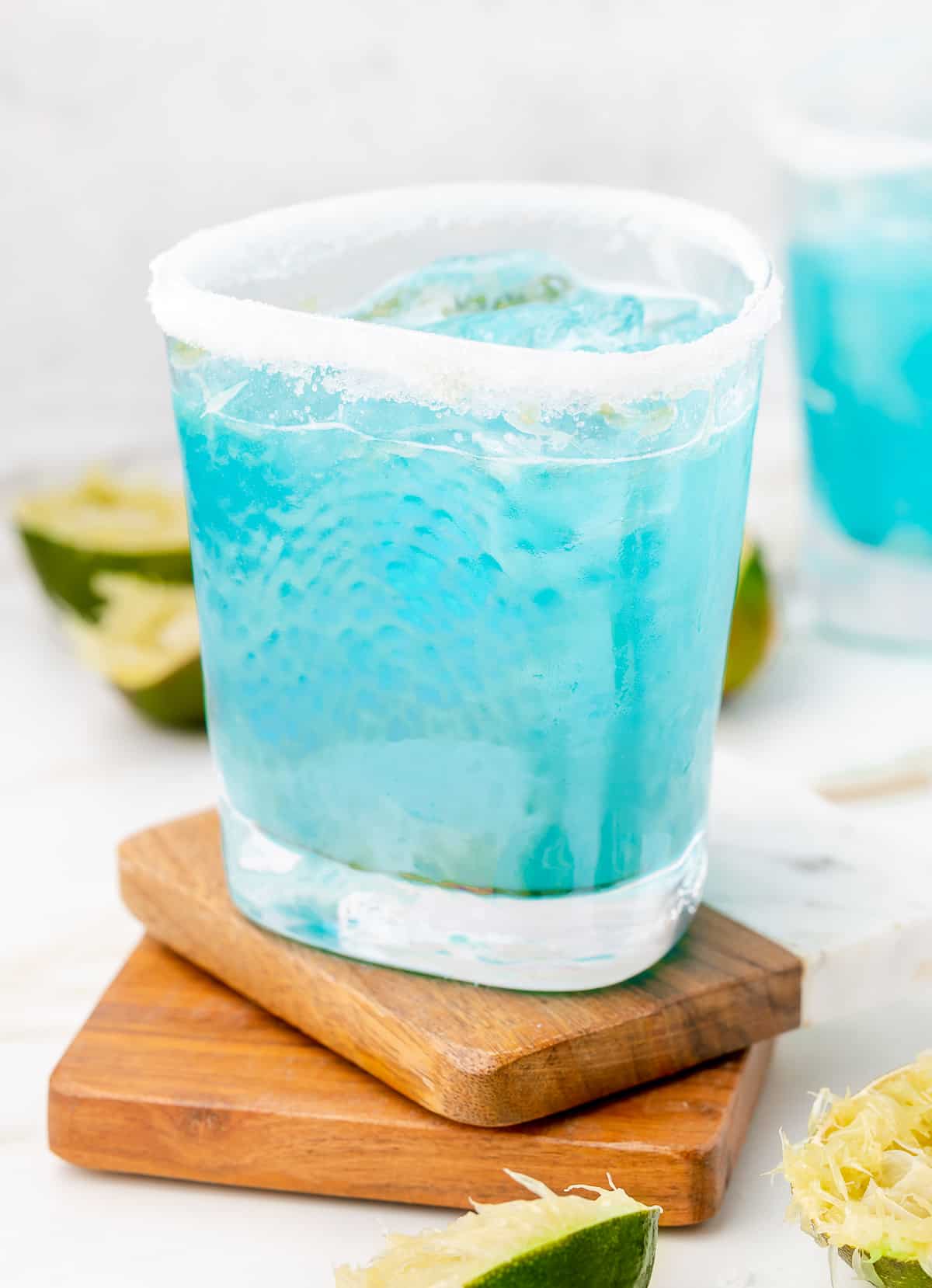 Margarita azul in a sugar rimmed glass, with limes for garnish.