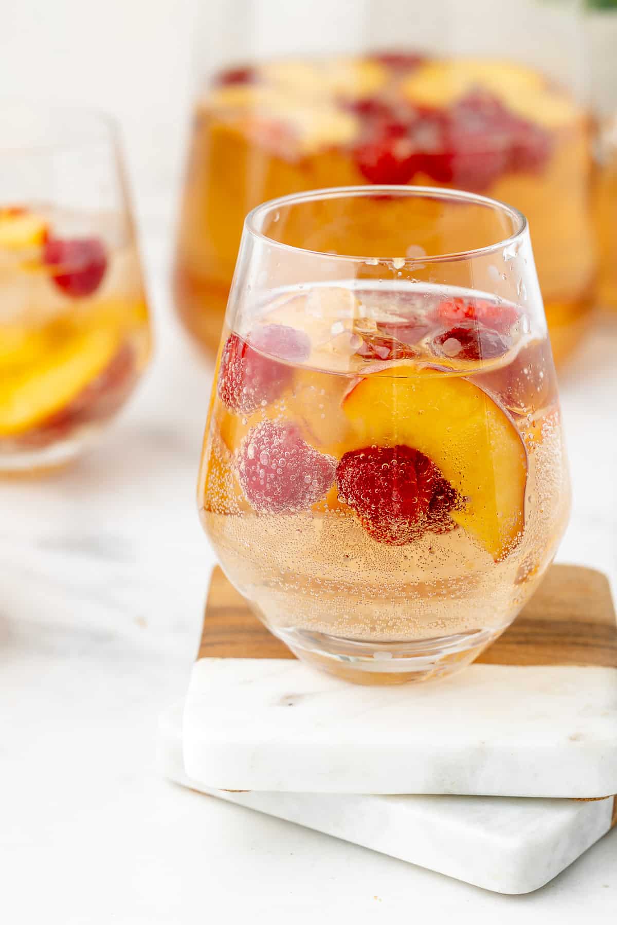 Sparkling rose sangria served in a wine glass, with a pitcher in the background.