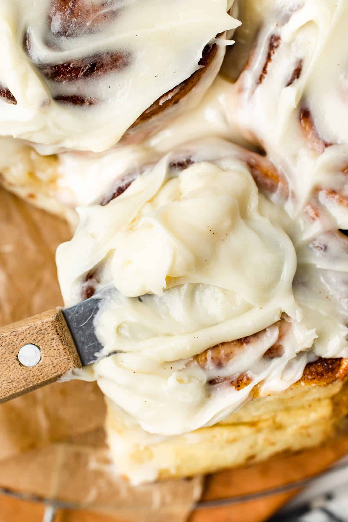 Image showing cinnamon roll frosting being spread onto a roll.