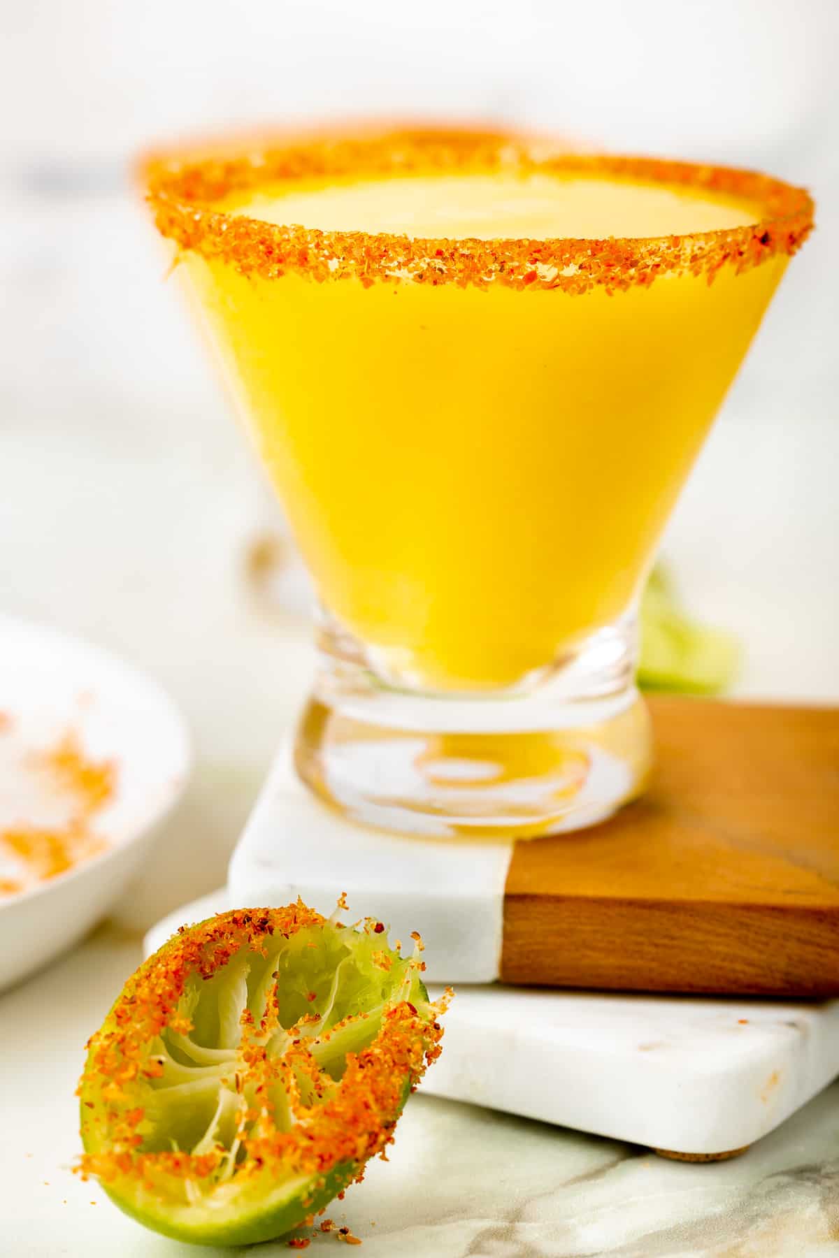 Yellow, frozen mangorita on top of two coasters, in the forefront a sqeezed lime with tajin seasoning around the edges