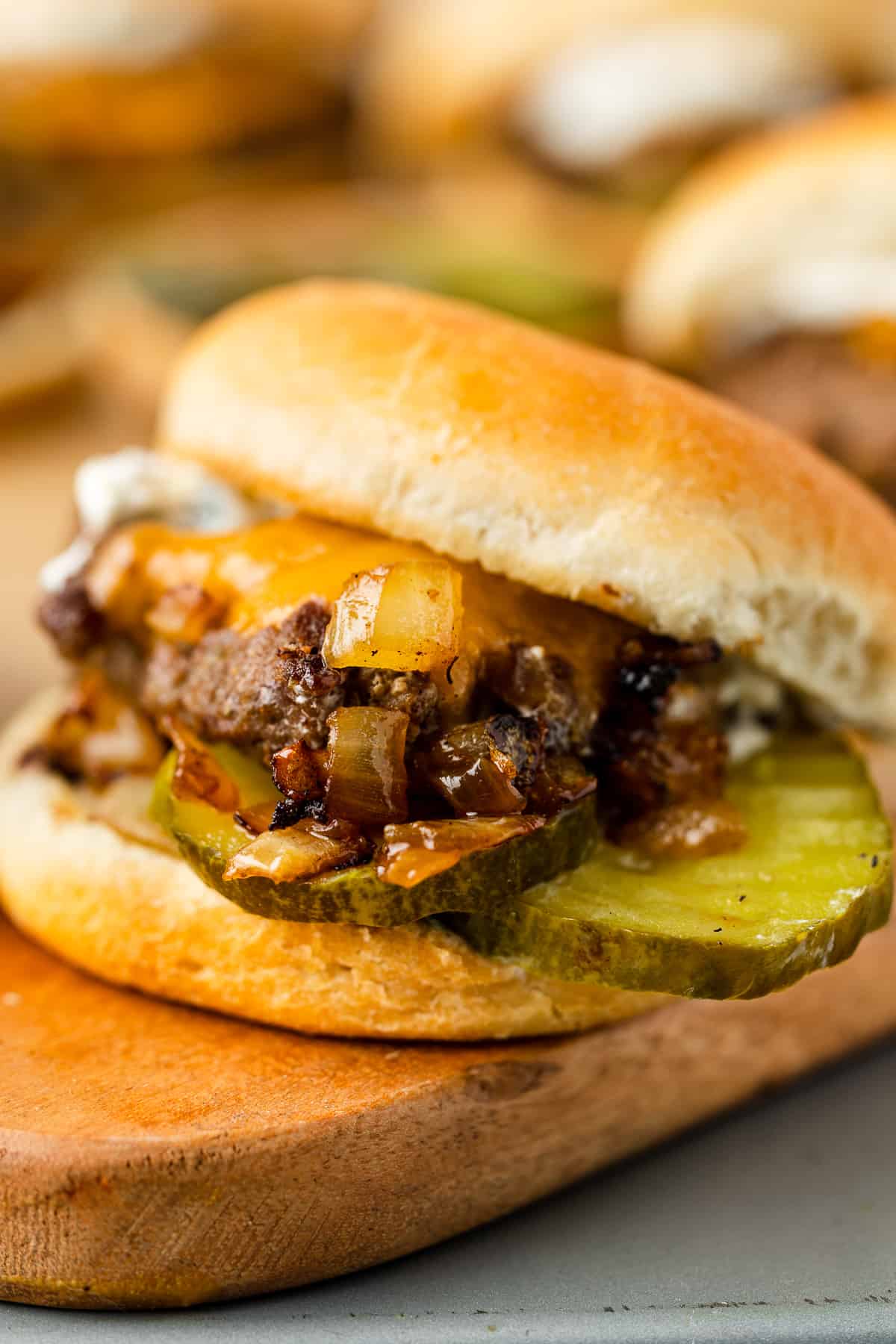 Up close photo of Grilled Onion Cheddar Slider with a pickle sticking out on a wooden board