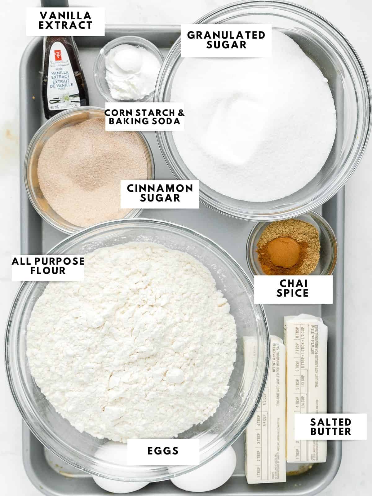 Photo of ingredients: granulated sugar, vanilla extract, corn starch & baking soda, cinnamon sugar, chai spice, all purpose flour, eggs, and salted butter