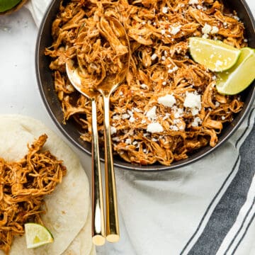 Shredded chicken tinga served in a bowl, with limes and cotija cheese.