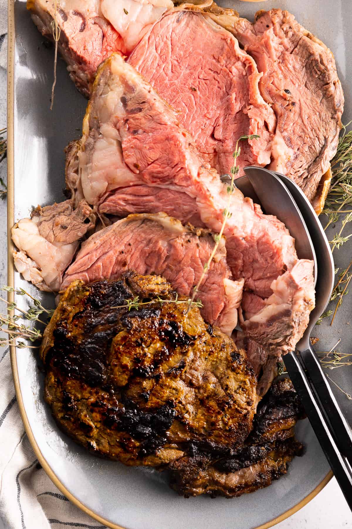 Sliced prime rib served on a platter, garnished with fresh thyme.