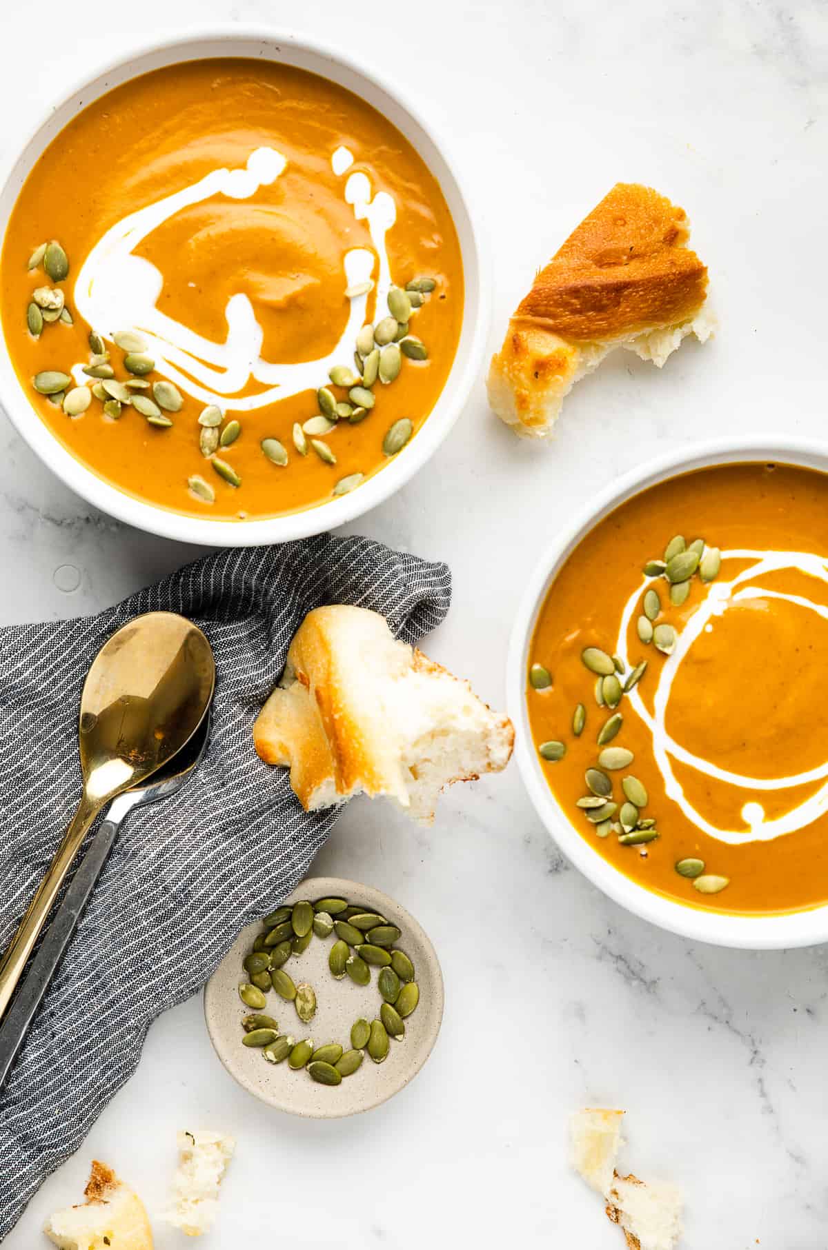 Two bowls of pumpkin soup, garnished with pumpkin seeds and served with bread.
