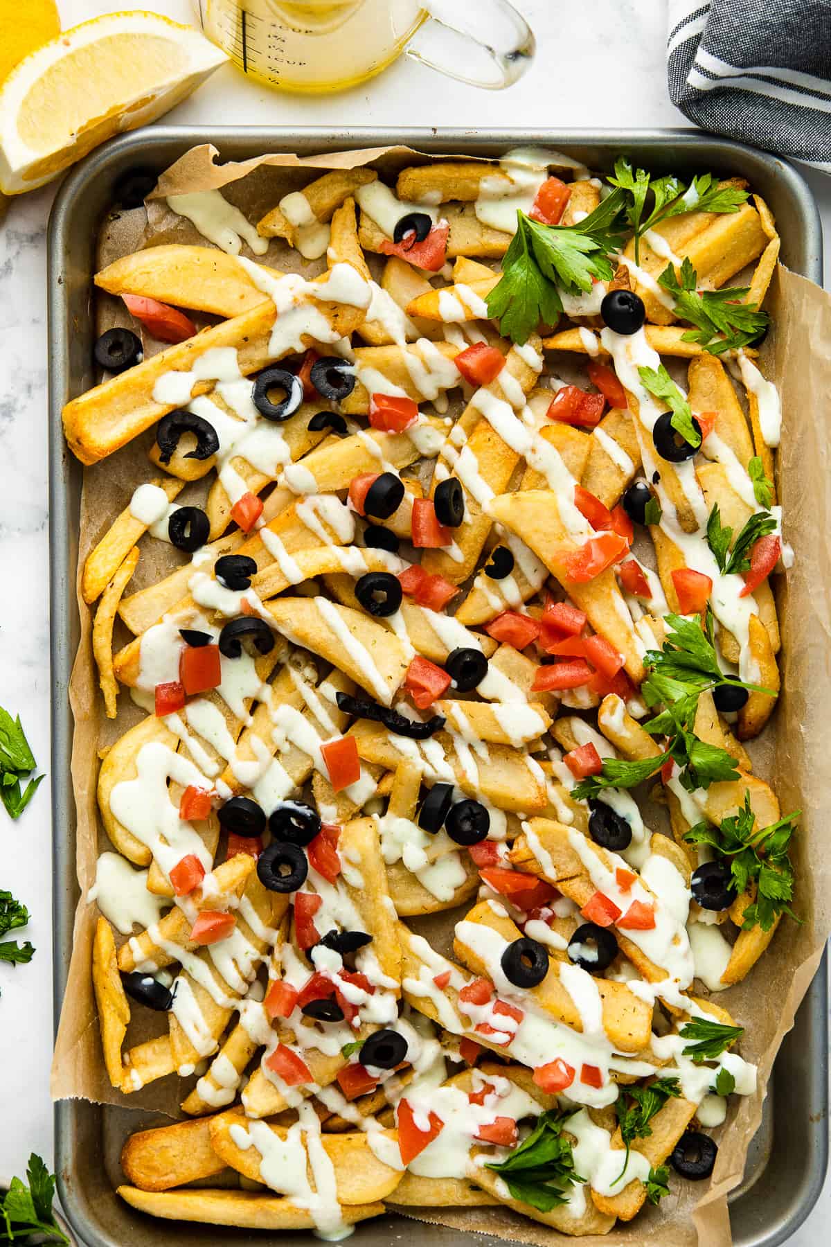 Loaded fries served on a sheet tray dressed with feta dressing and parsley.