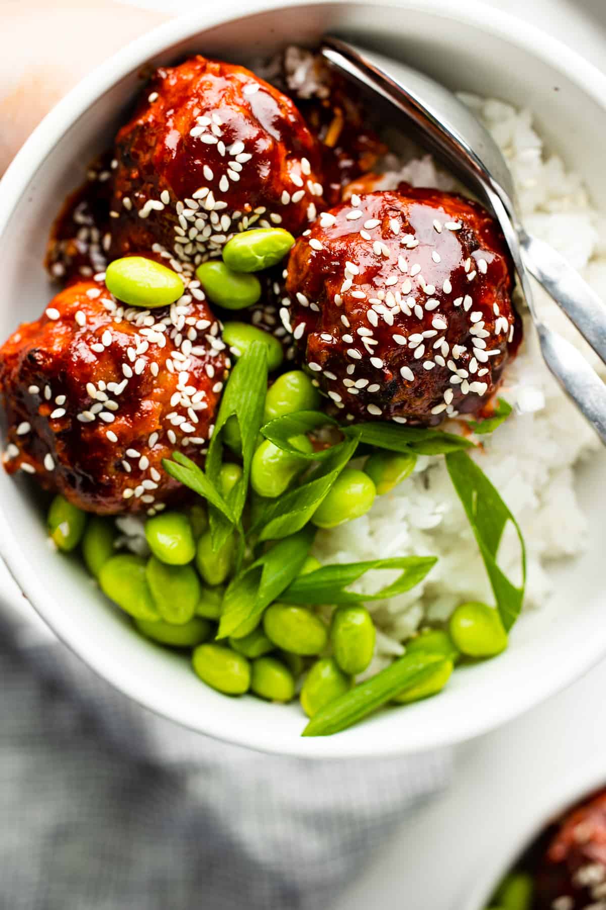 Korean meatballs in a bowl with jasmine rice, edamame and green onions, garnished with sesame seeds.