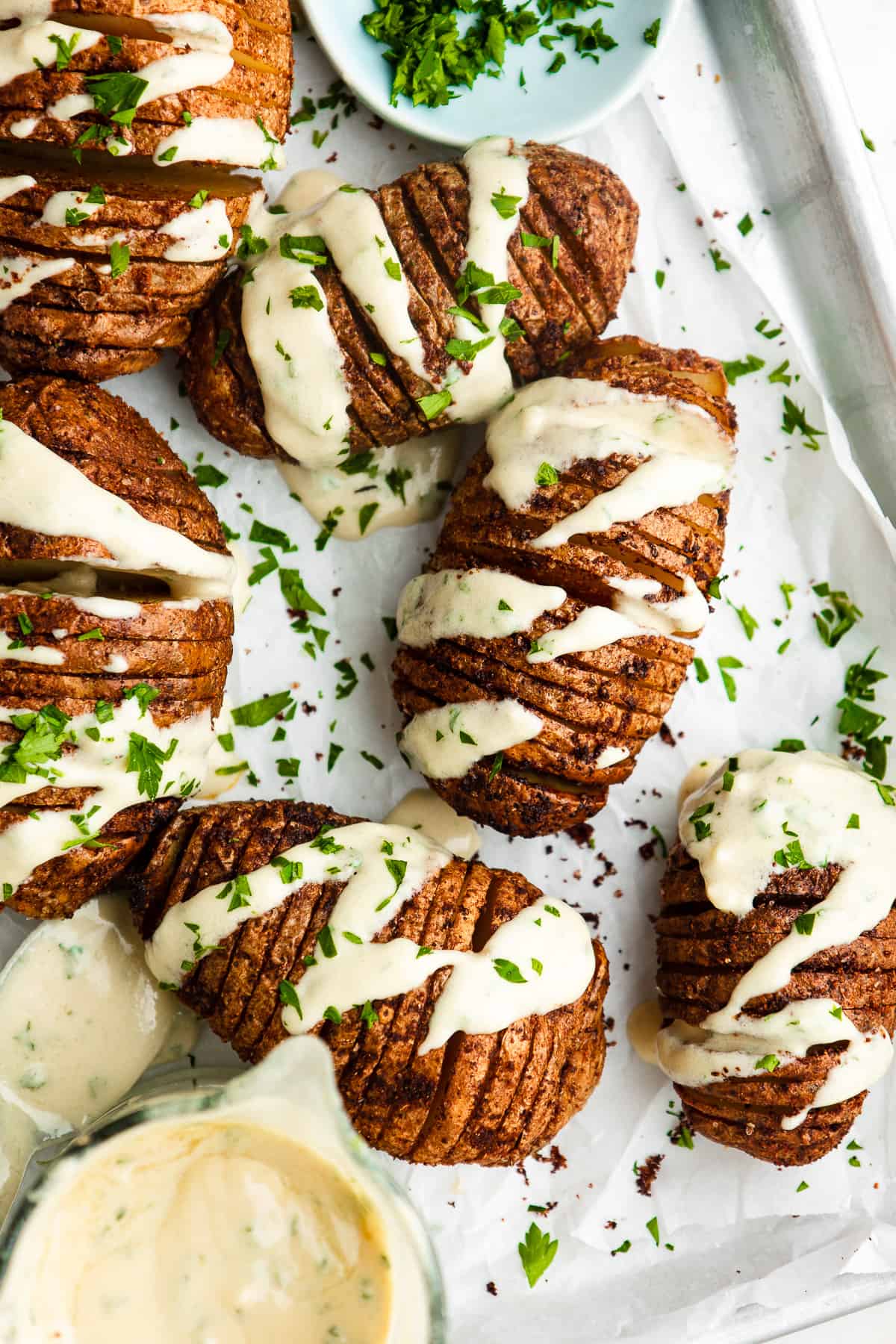 Hasselback potatoes served on a sheet tray, drizzled with tahini sauce.