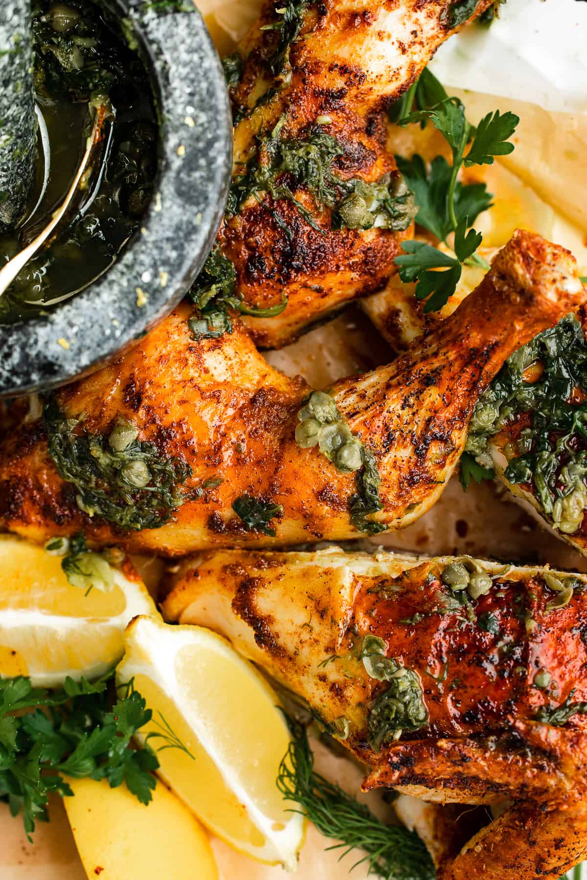 Cooked chicken arranged on a platter, dressed with herb sauce and lemons.