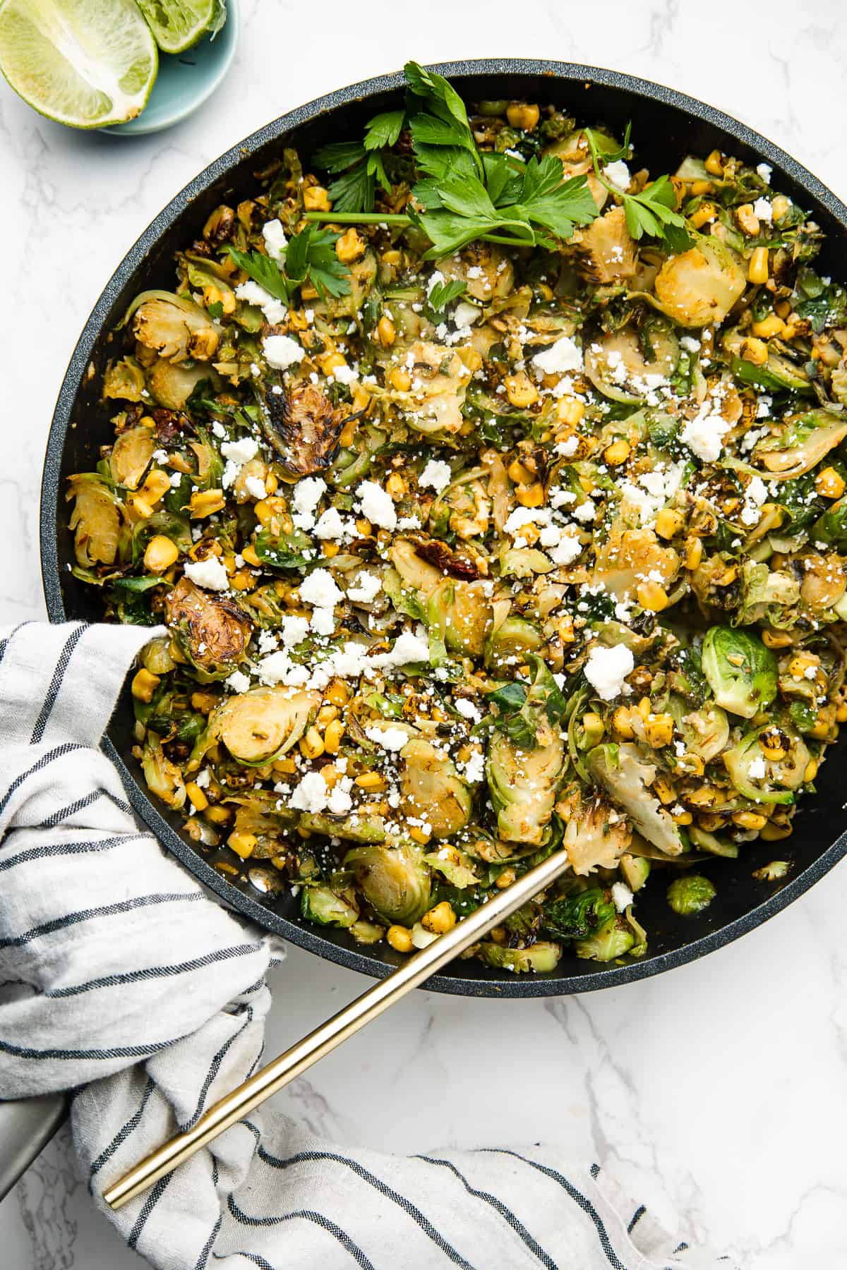 Mexican brussel sprouts in a skillet, garnished with cilantro and a side of lime. 