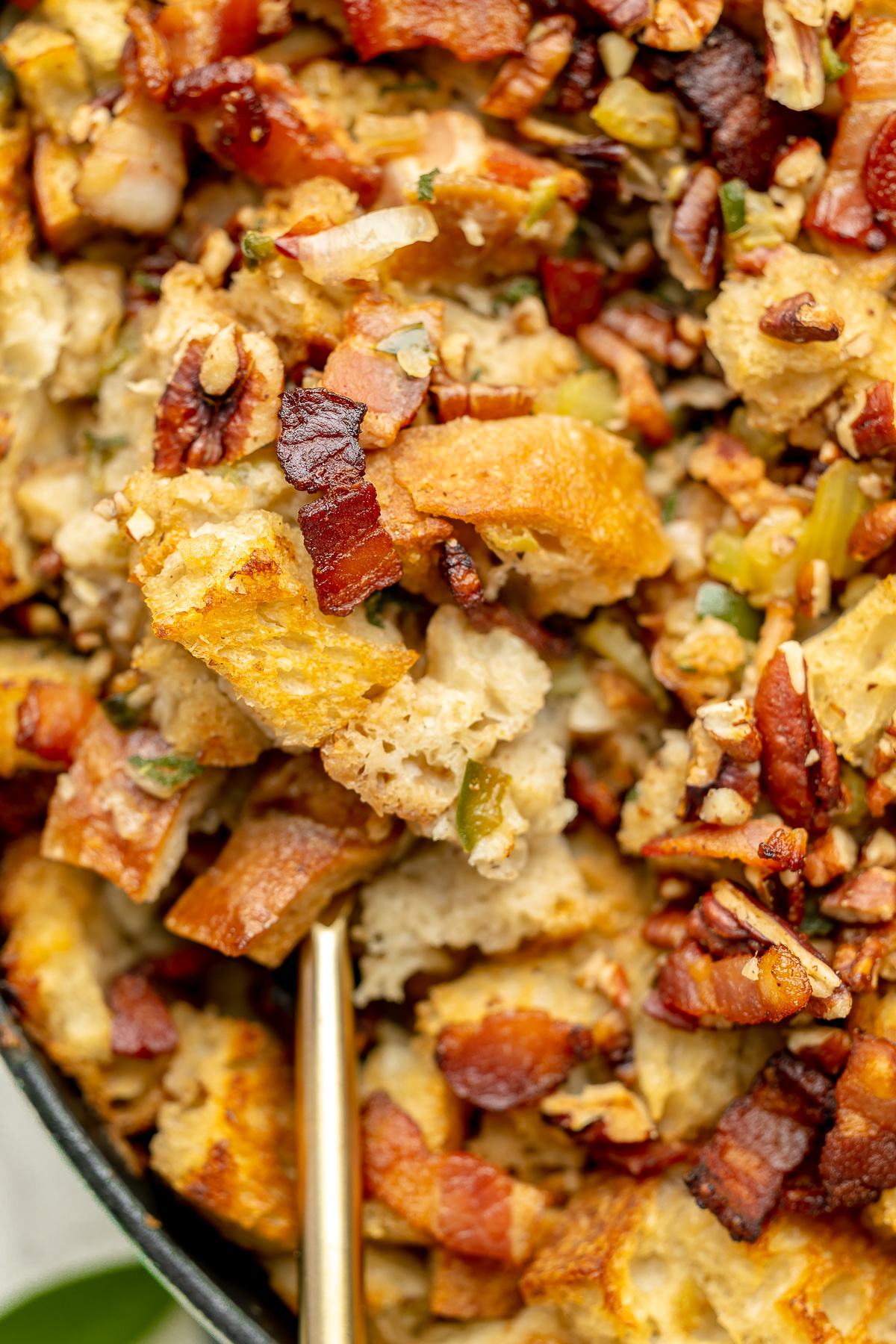 Large serving spoon scooping up sourdough stuffing, dressed with bacon and pecans.