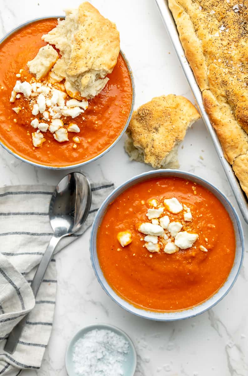 Tomato feta soup served in two bowls, with a piece of bread dipped into the bowl.