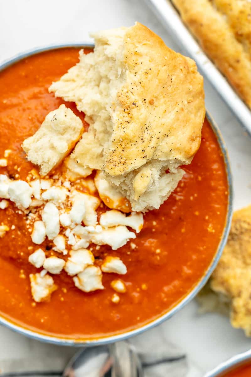 Close-up shot of tomato feta soup served with a piece of torn bread.