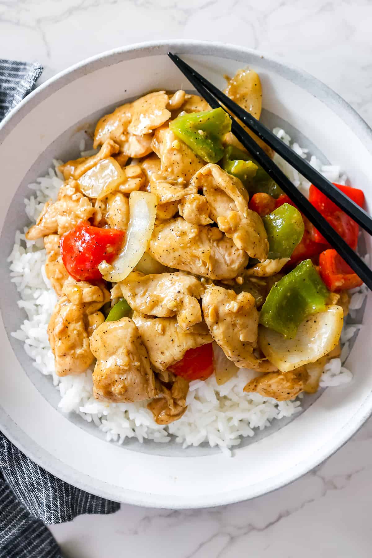 Finished black pepper chicken stir fry served in a bowl on top of jasmine rice, with chopsticks.