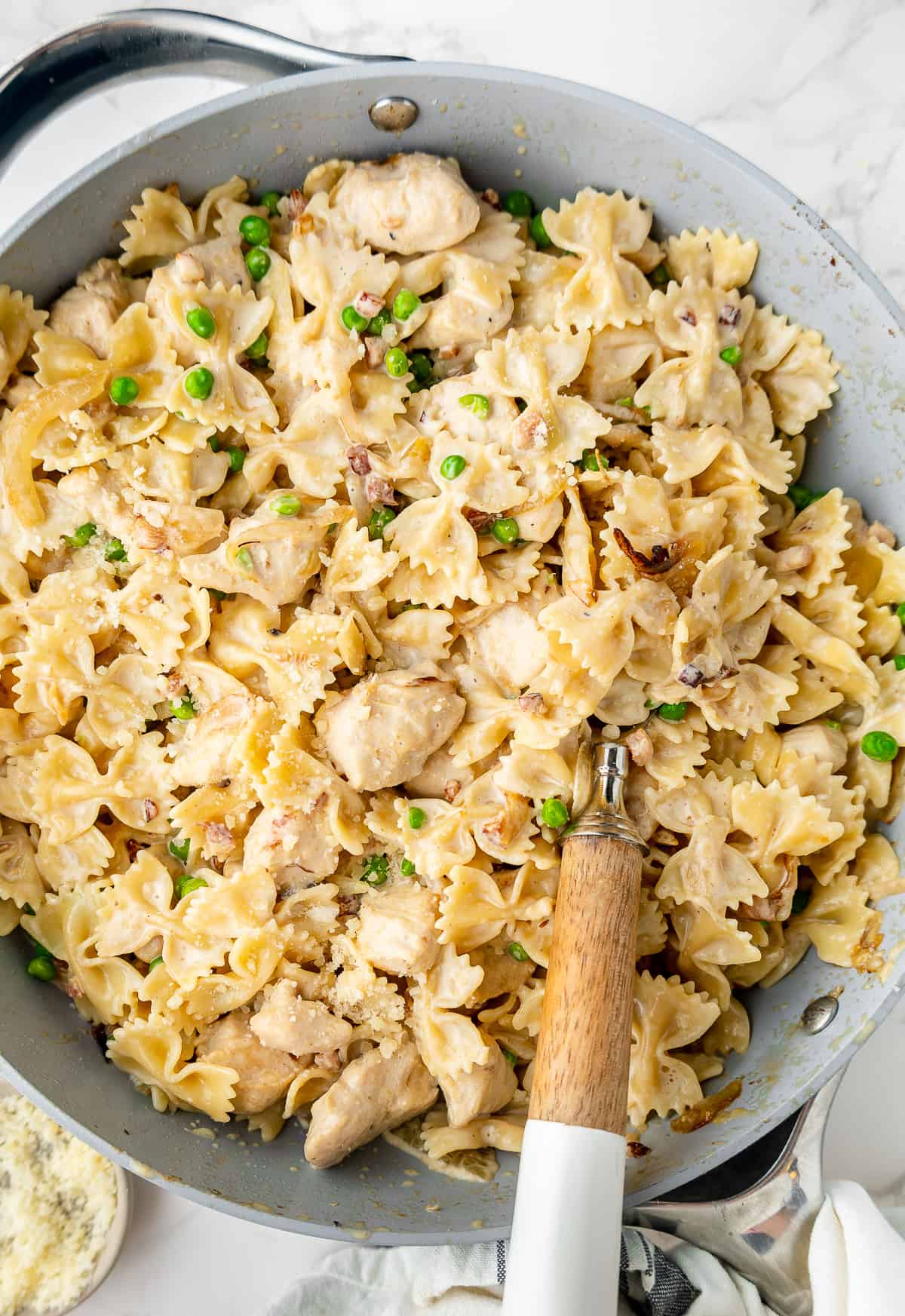 Finished farfalle with roasted garlic & chicken in a skillet, with a serving spoon.
