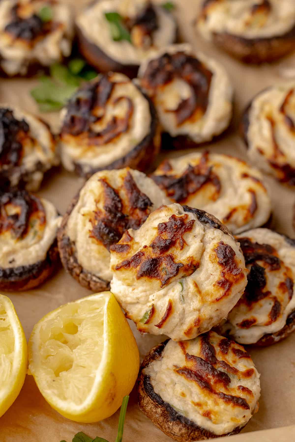 Baked stuffed mushroom neptune arranged on parchment paper, with squeezed lemons on the side. 