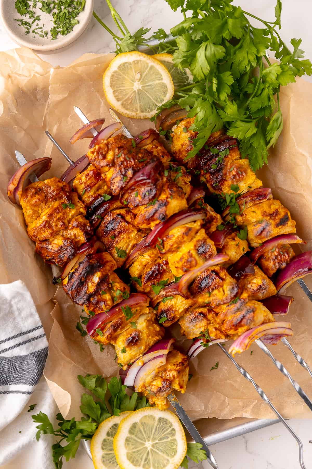 Skewers of shish taook served on parchment paper with fresh parsley to garnish. 
