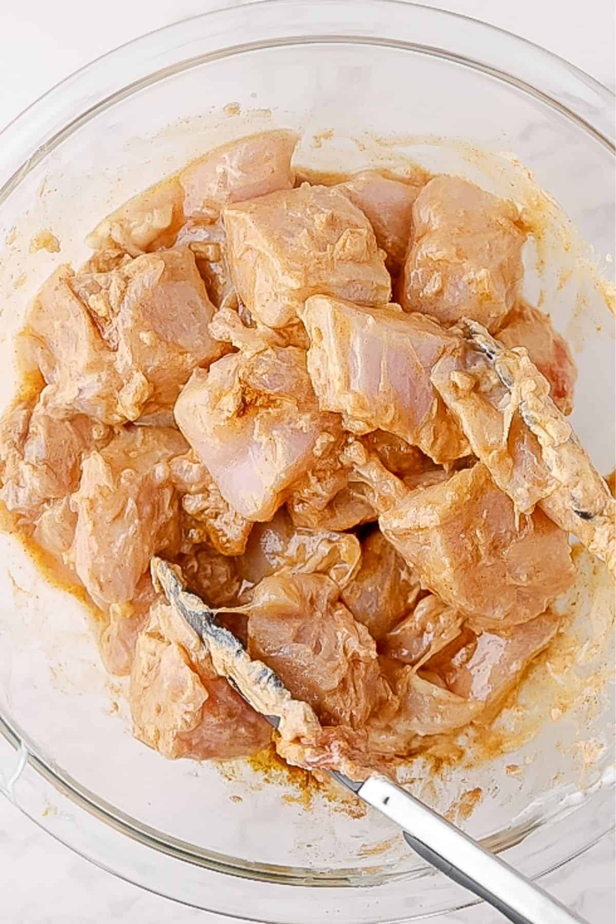 Chicken mixed in marinade, in a mixing bowl.