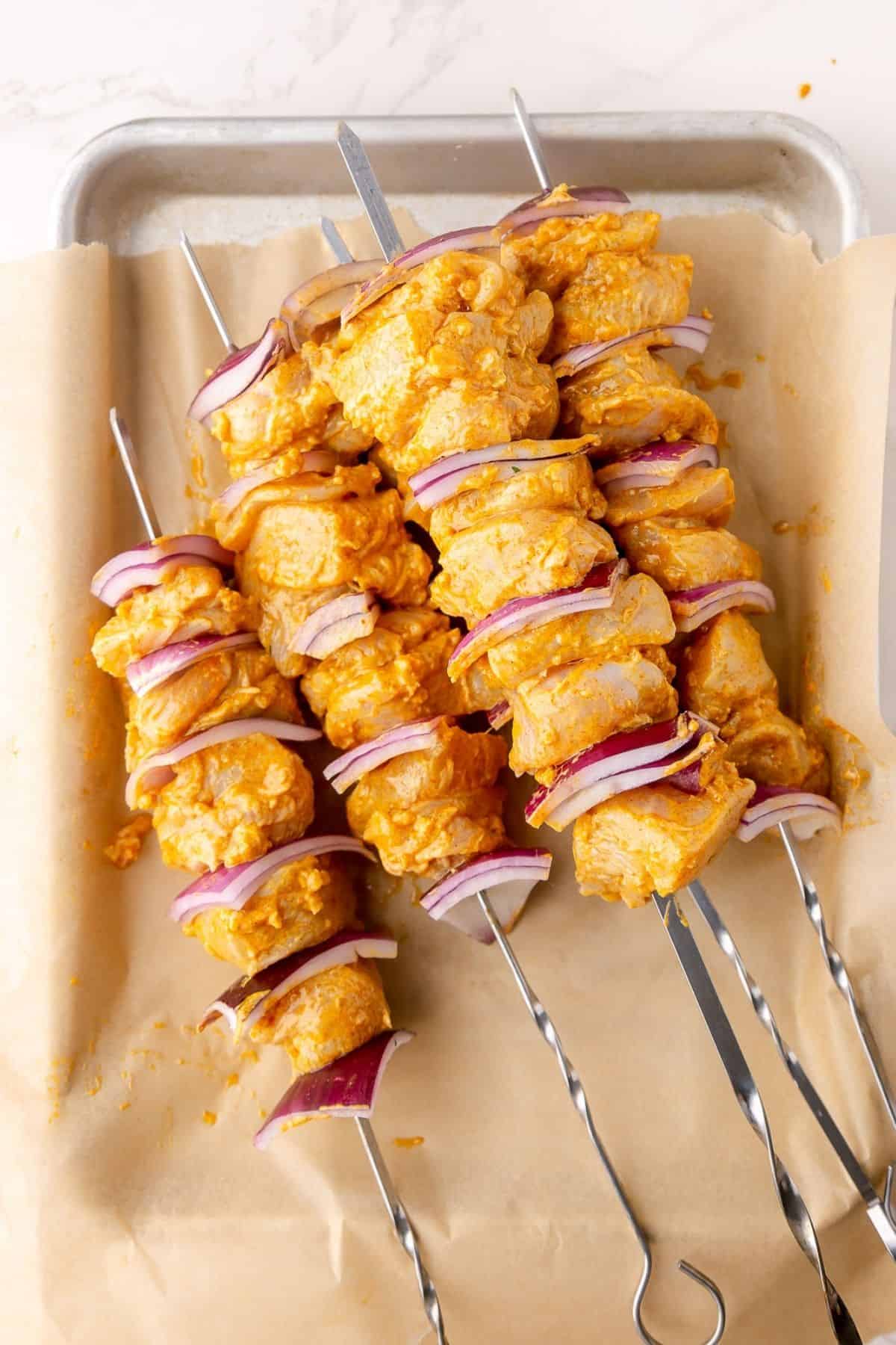 Skewered chicken with red onions, laid out on a sheet tray.