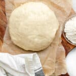 A ball of pizza dough on a parchment-lined wooden paddle.