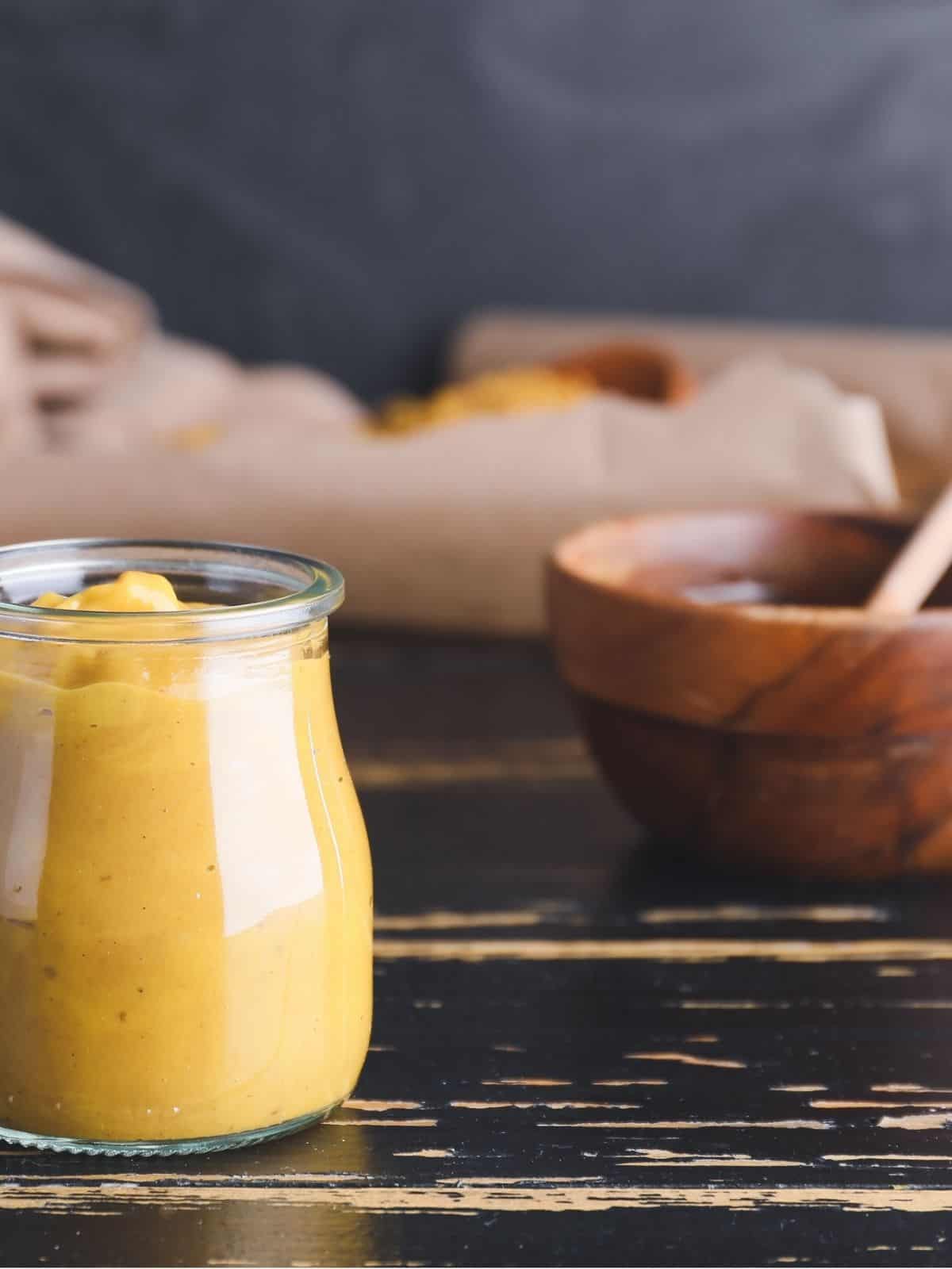 Honey mustard in a jar, with a bowl of honey in the background.