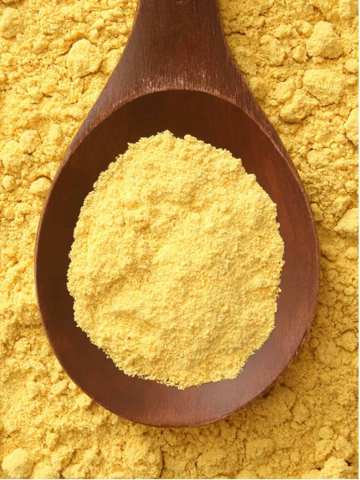 A spoon of mustard powder laid on top of a background of mustard powder.