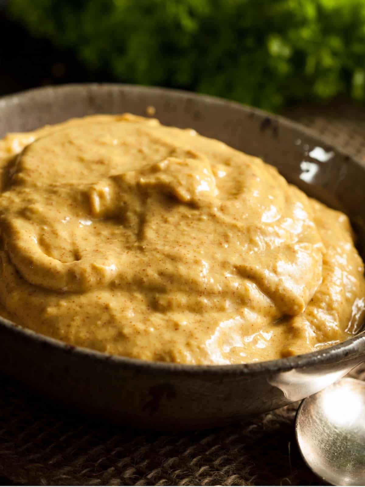 Prepared brown mustard in a bowl, with a spoon in the foreground.