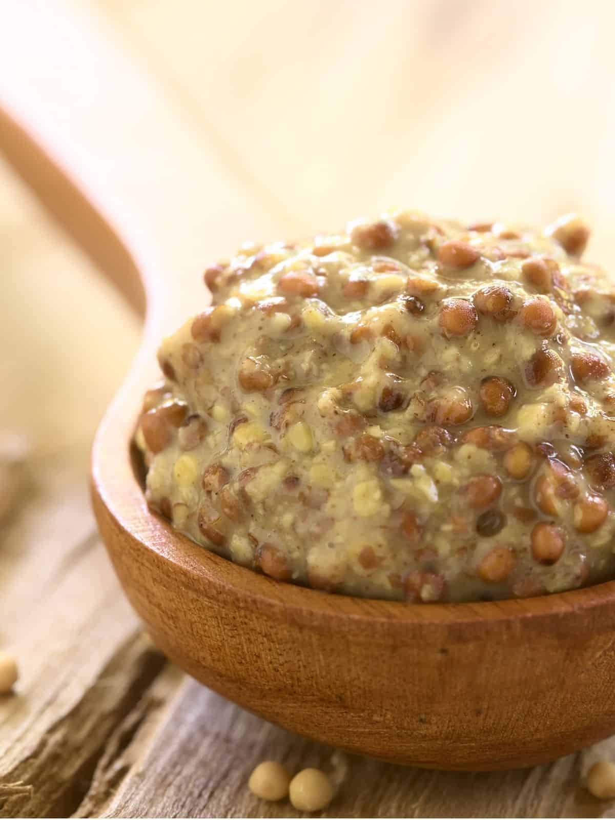 A close-up shot of whole-grain mustard in a large wooden spoon.