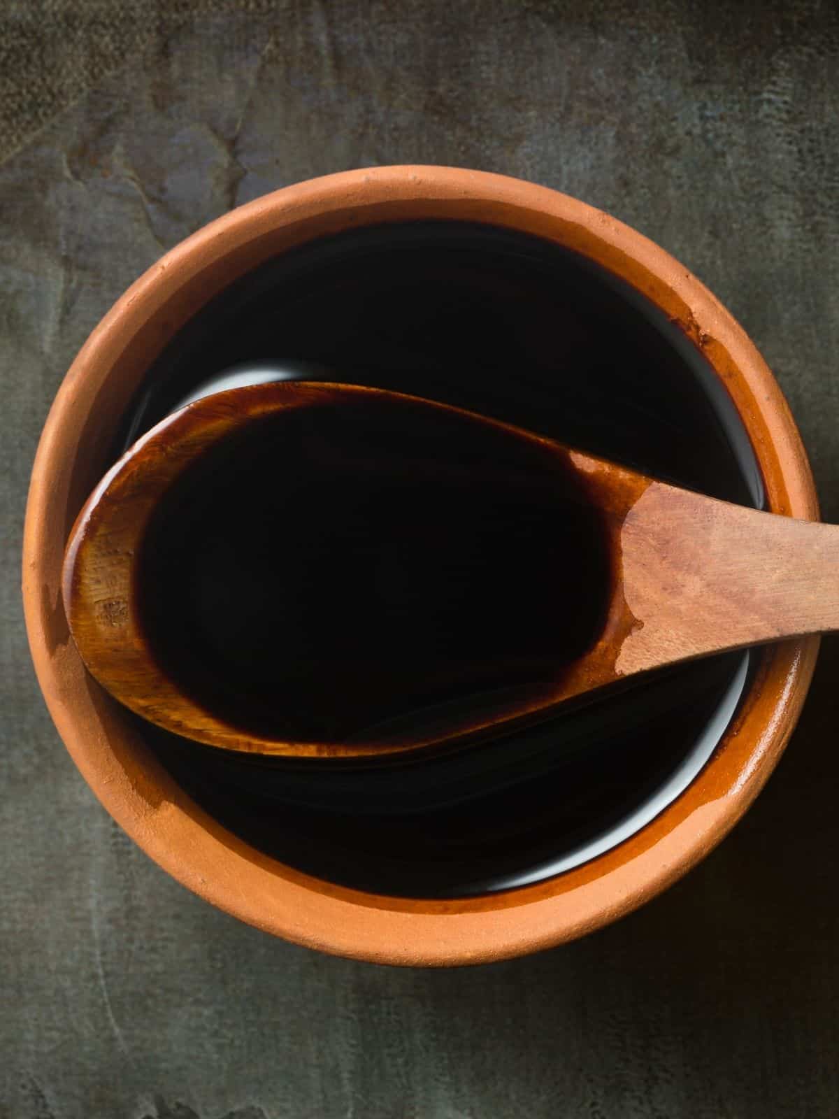 A wooden bowl and a wooden spoon showing the consistency of Worcestershire sauce.