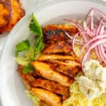 Sliced harissa chicken served over yellow rice, garnished with red onions.