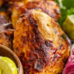 Citrus marinated grilled chicken, arranged on a platter with fresh limes and pickled red onions.