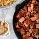 Benihana hibachi steak cubes in a cast iron skillet, with fried rice in a serving dish in the background.
