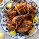 Grilled nando's chicken served on a platter, with lime wedges to garnish.