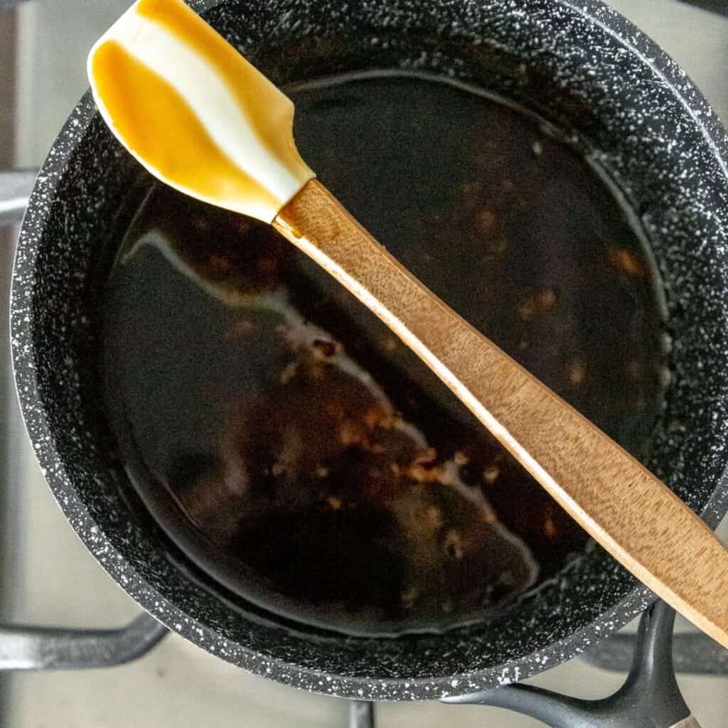 Teriyaki sauce in a small sauce pan, with a spoon showing the consistency of the sauce. 
