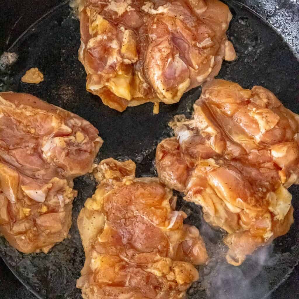 Chicken thighs cooking in a cast iron skillet, skin down. 