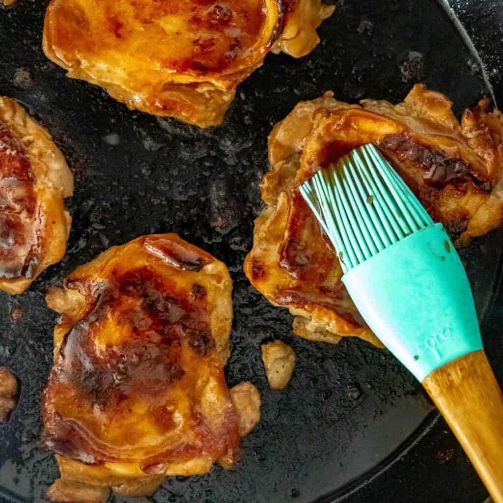 Basting chicken thighs with teriyaki sauce, in a cast iron skillet. 